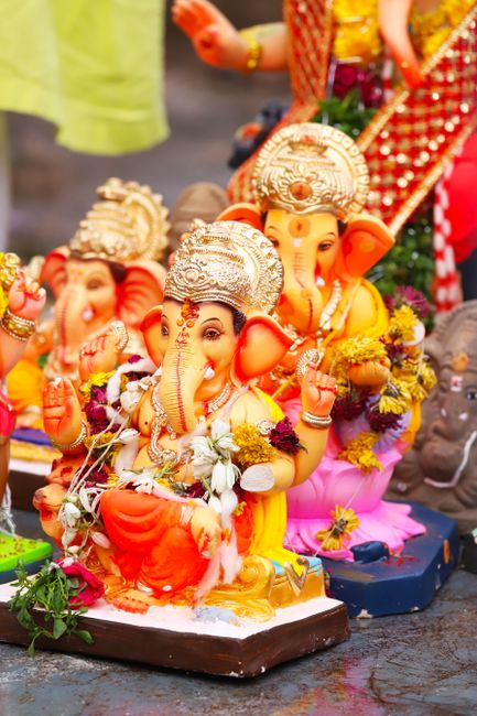 A brightly lit, colorful scene featuring a large illuminated installation of Lord Ganesha, the Hindu deity with an elephant head, seated on a decorated platform. The display is set against a multi-tie